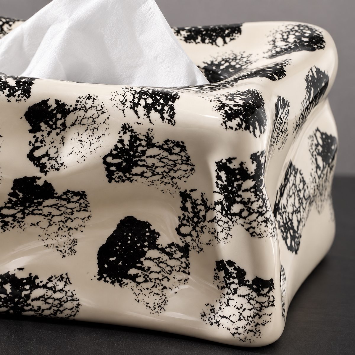 Close view of broken black ink impressions across the folded cream ceramic surface and wavy top edge.