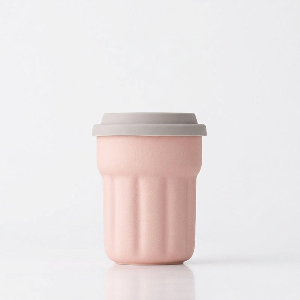 Blush pink fluted ceramic travel mug with gray sliding lid on a white background