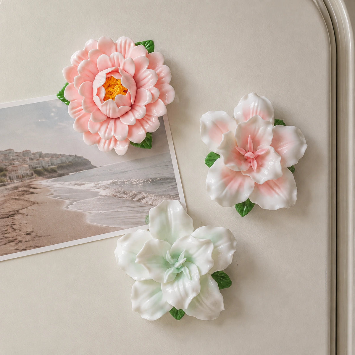 Blush Garden ceramic flower magnets framing a seaside photo on an ivory fridge.