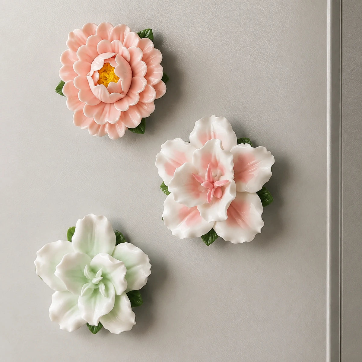 Blush Garden trio of pink and pale-green ceramic flower magnets in an open zig-zag on a grey metal door.