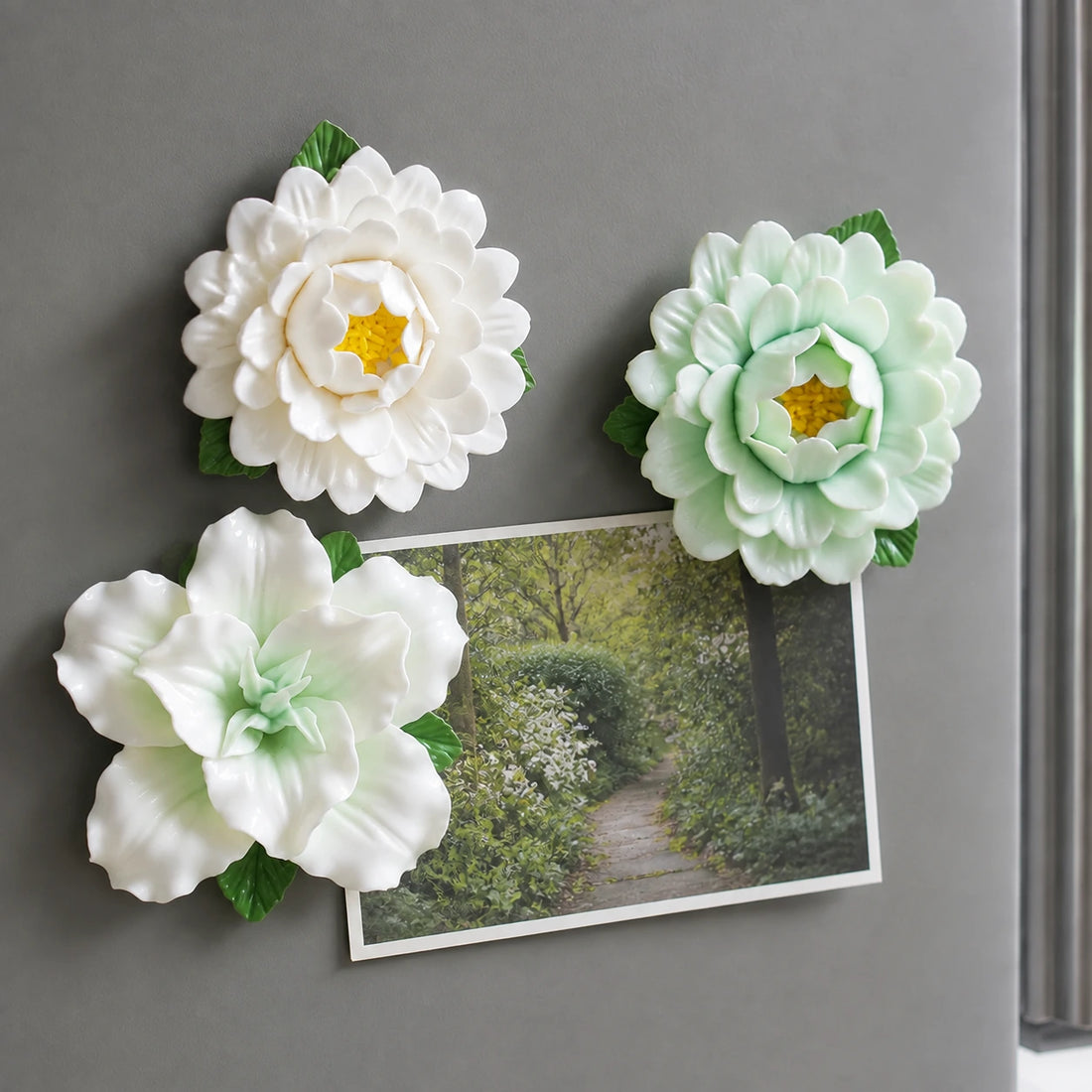 Sage & Ivory ceramic flower magnets framing a garden-path photo on a graphite-grey fridge.