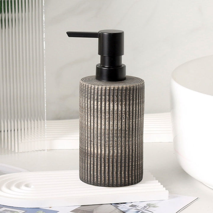 Dark charcoal ribbed ceramic soap dispenser with black pump facing left, on a white tray beside a fluted container.