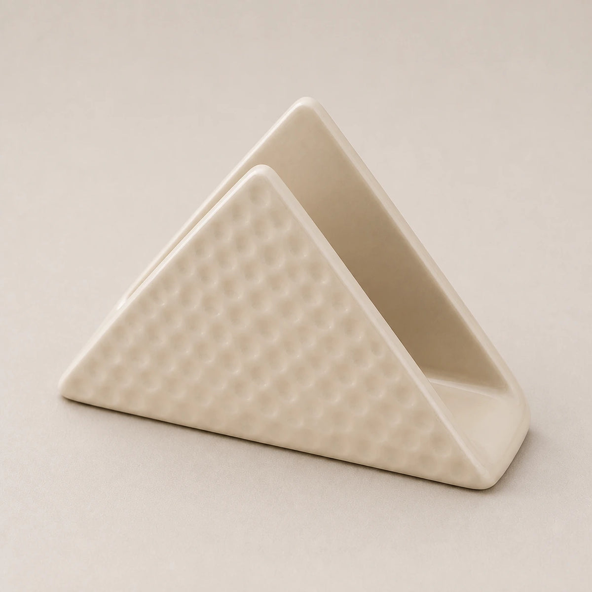 Angled close view of a beige ceramic napkin holder showing two walls, one slot, and dimpled relief