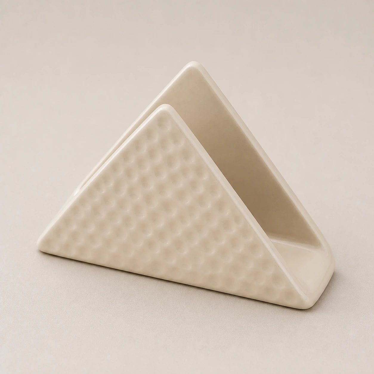 Angled close view of a beige ceramic napkin holder showing two walls, one slot, and dimpled relief