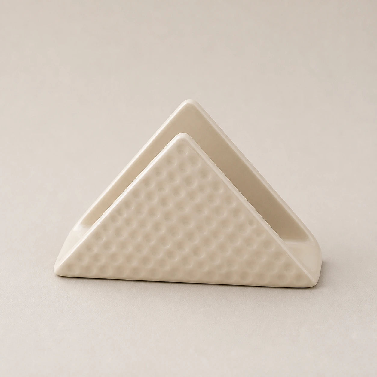 Light beige triangular ceramic napkin holder with dimpled outer panels