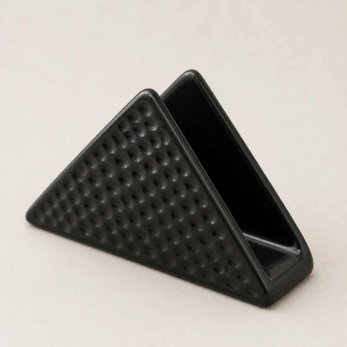 Angled close view of a black ceramic napkin holder showing two walls, one slot, and dimpled relief