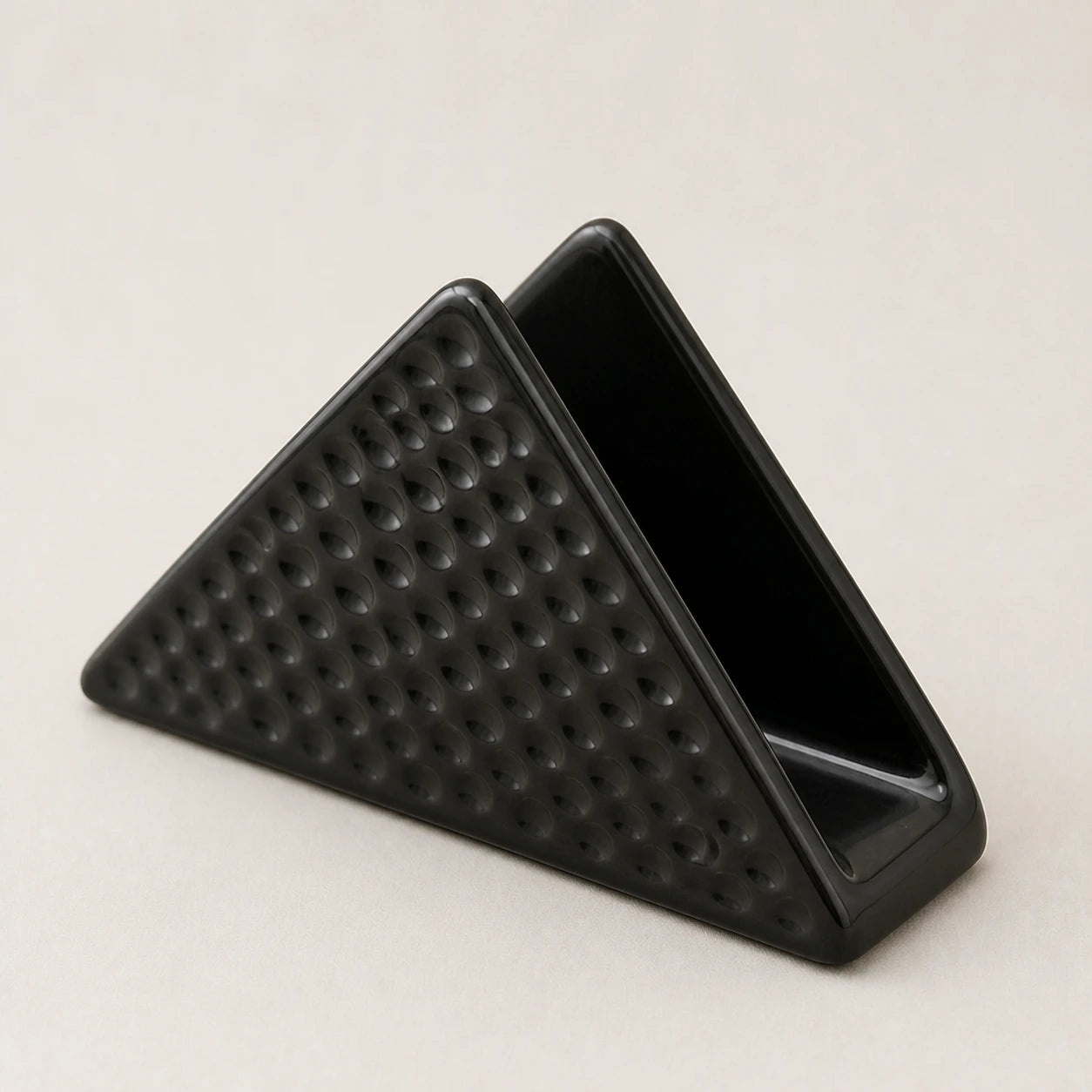 Angled close view of a black ceramic napkin holder showing two walls, one slot, and dimpled relief