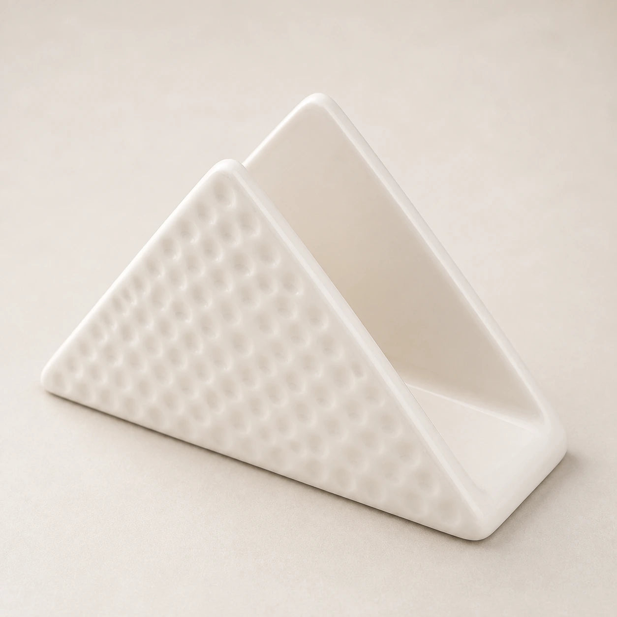 Angled close view of a white ceramic napkin holder showing two walls, one slot, and dimpled relief