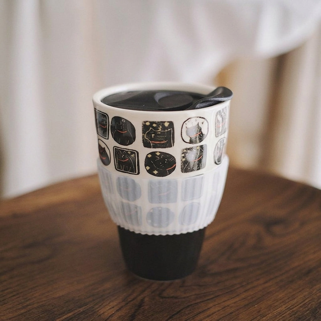 Nocturnal feline ceramic travel mug with black lid, clear sleeve and black base on wood table