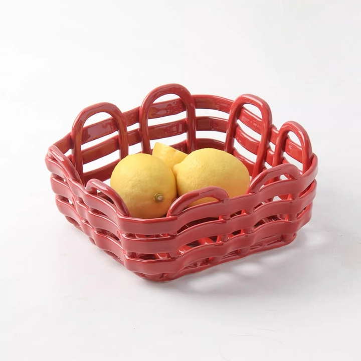 Glossy red square ceramic basket with open looped sides holding yellow lemons on a white studio background.