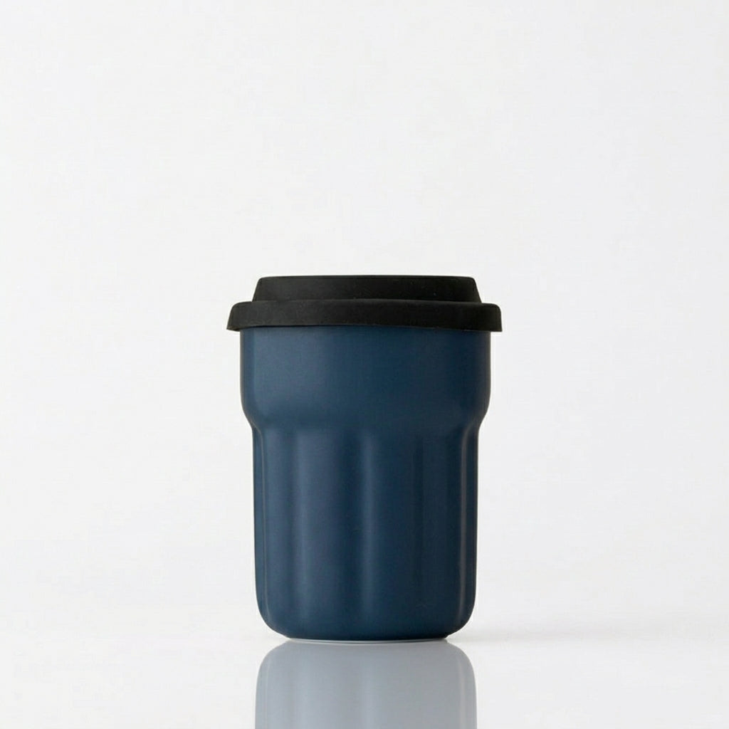 Navy blue fluted ceramic travel mug with black sliding lid on a white background