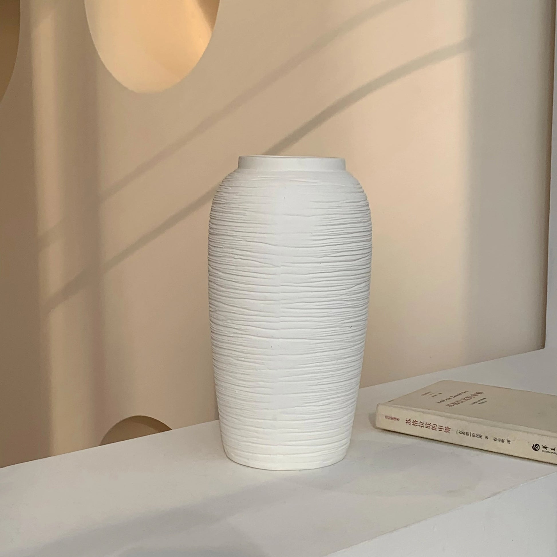 White textured ceramic vase on table next to a closed book with Asian characters
