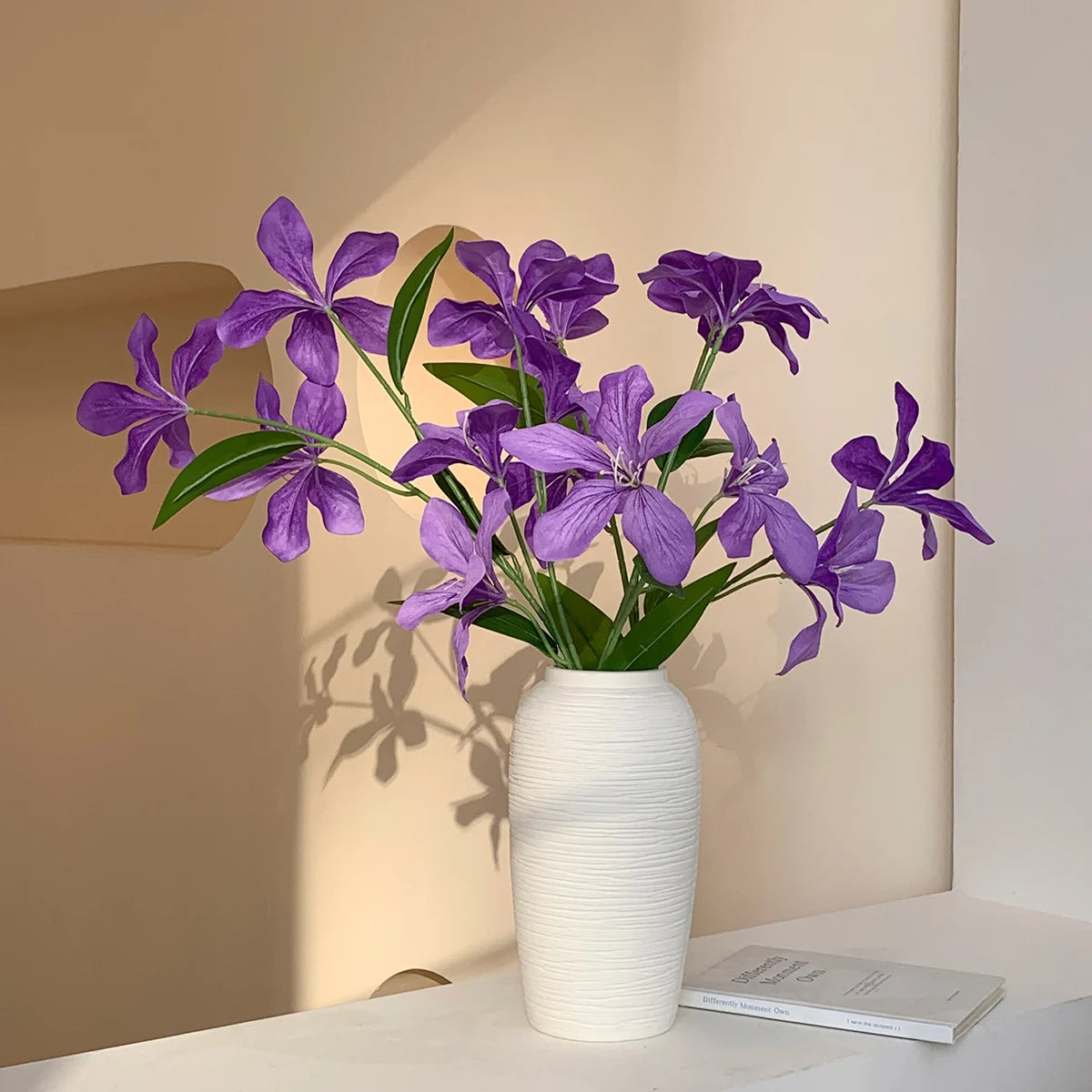 Purple flowers in a textured white ceramic vase on a white tabletop with a minimalist beige background