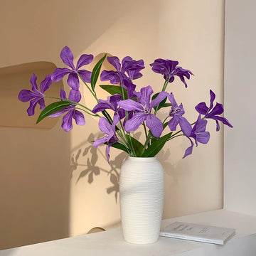 Purple flowers in a textured white ceramic vase on a white tabletop with a minimalist beige background