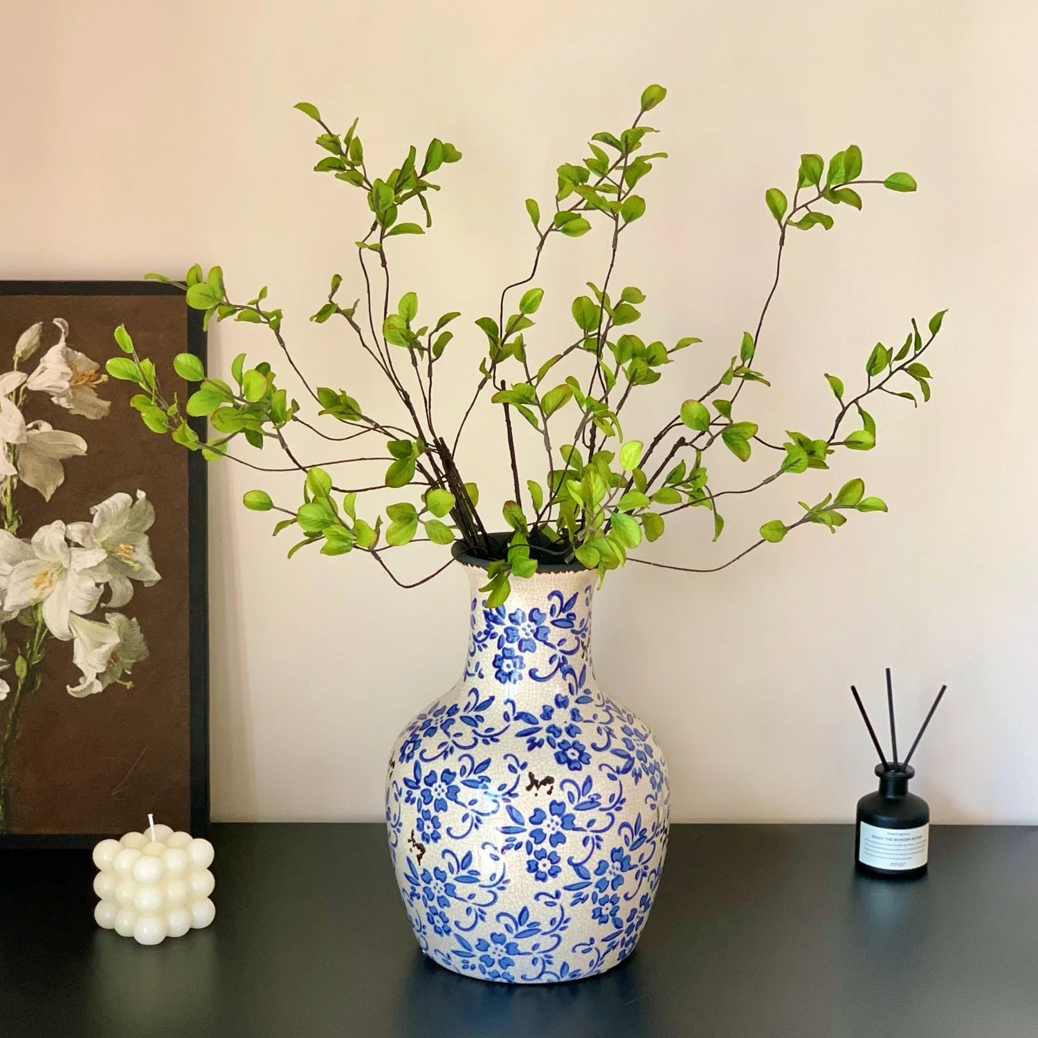 Blue and white floral ceramic vase with green leafy branches on black surface