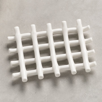 Empty white branch-grid ceramic soap dish on pale warm stone