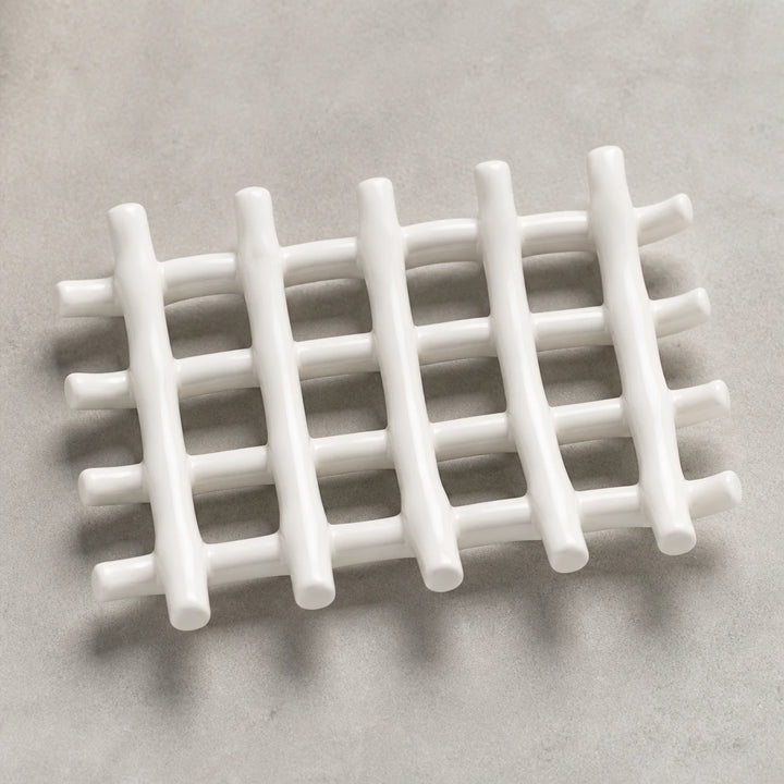 Empty white branch-grid ceramic soap dish on pale warm stone