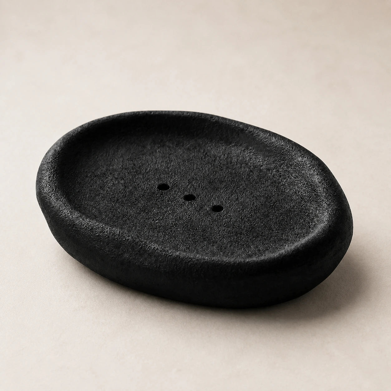 Empty black Vulcanized Obsidian ceramic soap dish on pale warm stone
