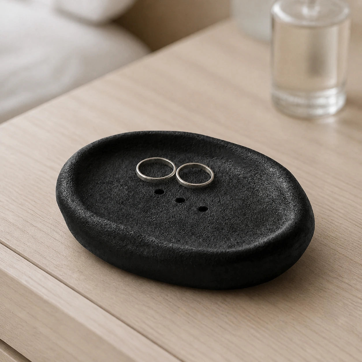 Black Vulcanized Obsidian ceramic dish holding two silver rings on a vanity