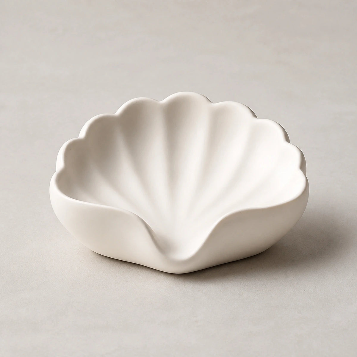 Pearl white scallop-shell ceramic soap dish on a light stone background