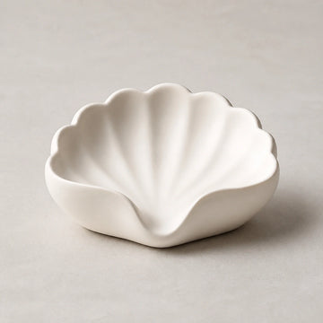 Pearl white scallop-shell ceramic soap dish on a light stone background