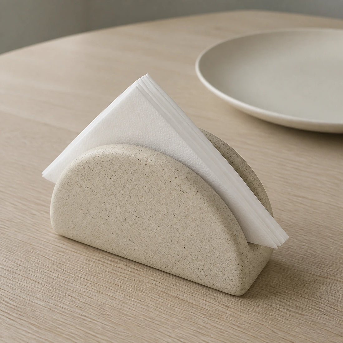 Speckled half-moon ceramic napkin holder with paper napkins on a dining table