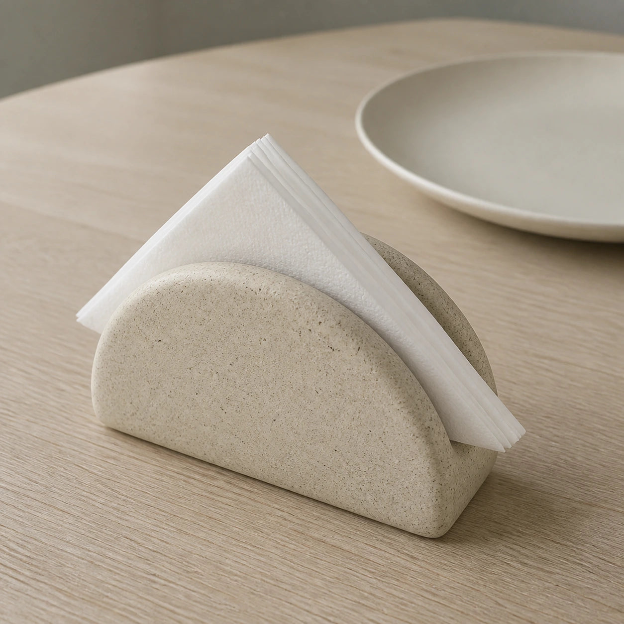 Speckled half-moon ceramic napkin holder with paper napkins on a dining table