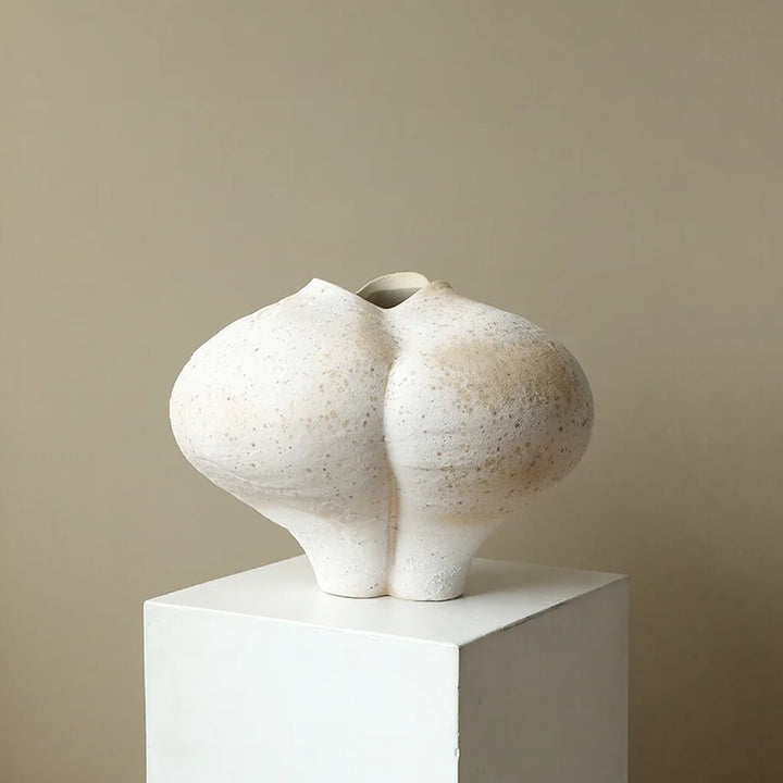 Off-white sculptural body vase with two rounded lobes, a deep central groove, wavy top opening, and two narrow supports.