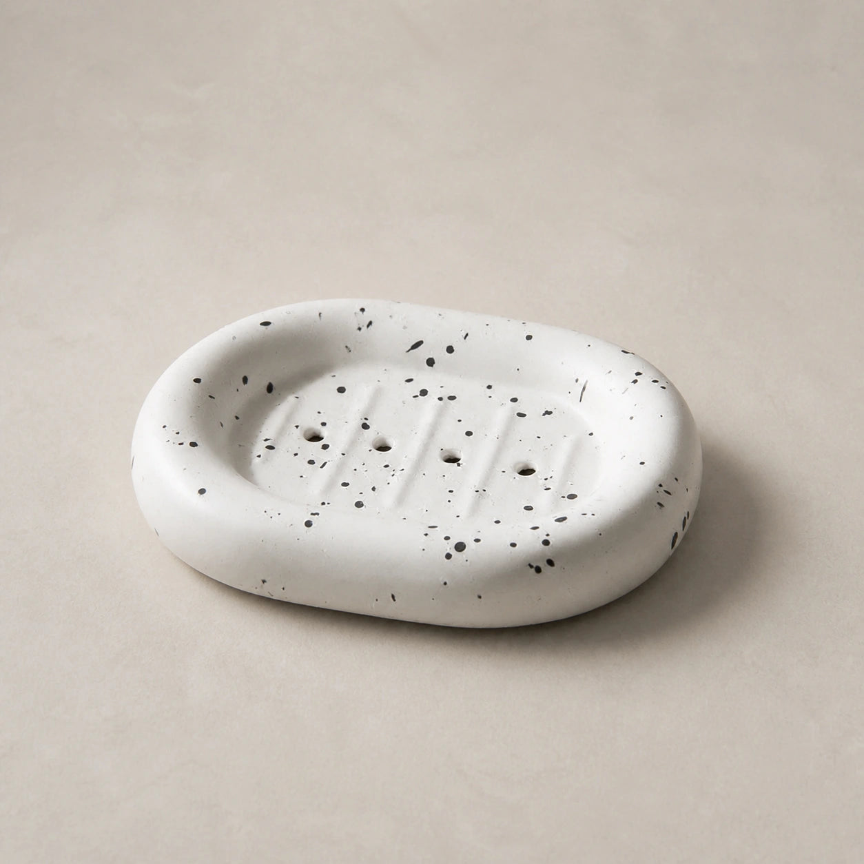 Ink splatter white rounded ceramic soap dish on a light stone background