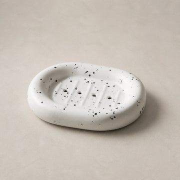 Ink splatter white rounded ceramic soap dish on a light stone background