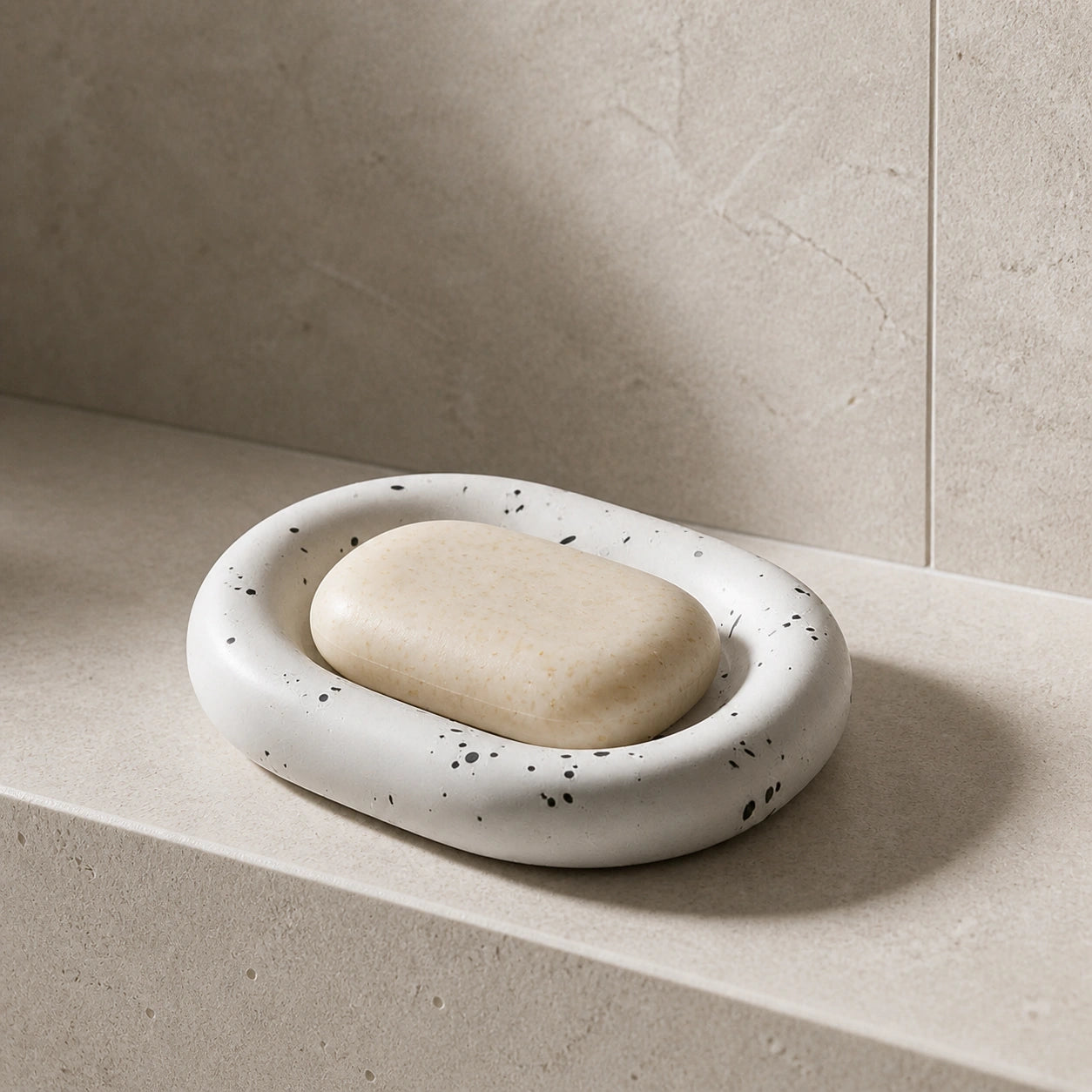 Ink splatter white ceramic soap dish with soap on a light stone bath shelf