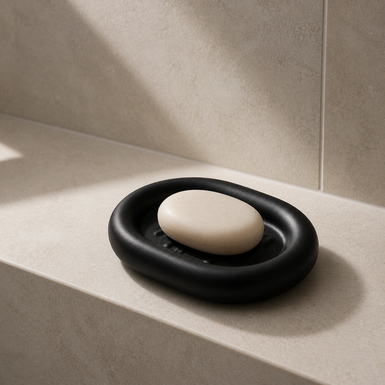 Matte black ceramic soap dish with soap on a light stone bath shelf