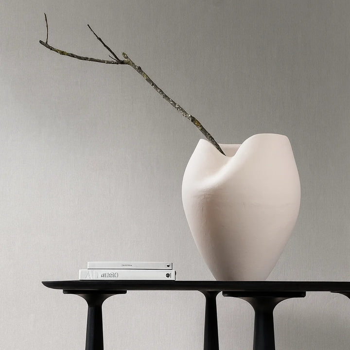 Large off-white ceramic vase holding a dark forked branch, styled on a black table beside two pale books.