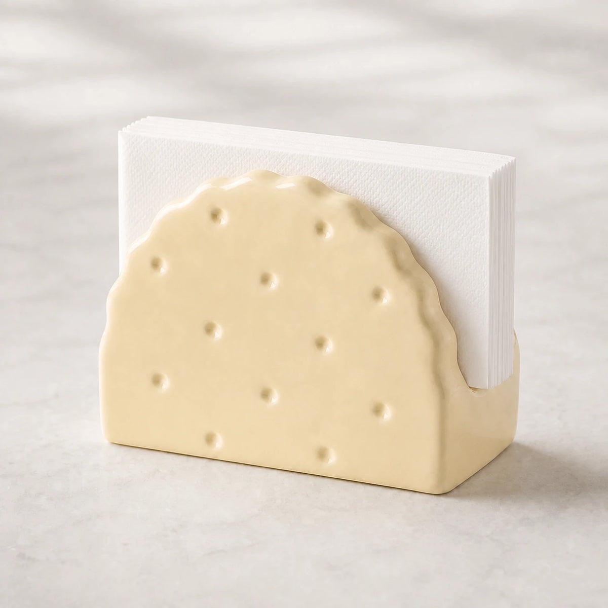 Butter Cream Soda Cracker ceramic napkin holder with folded white napkins on pale stone