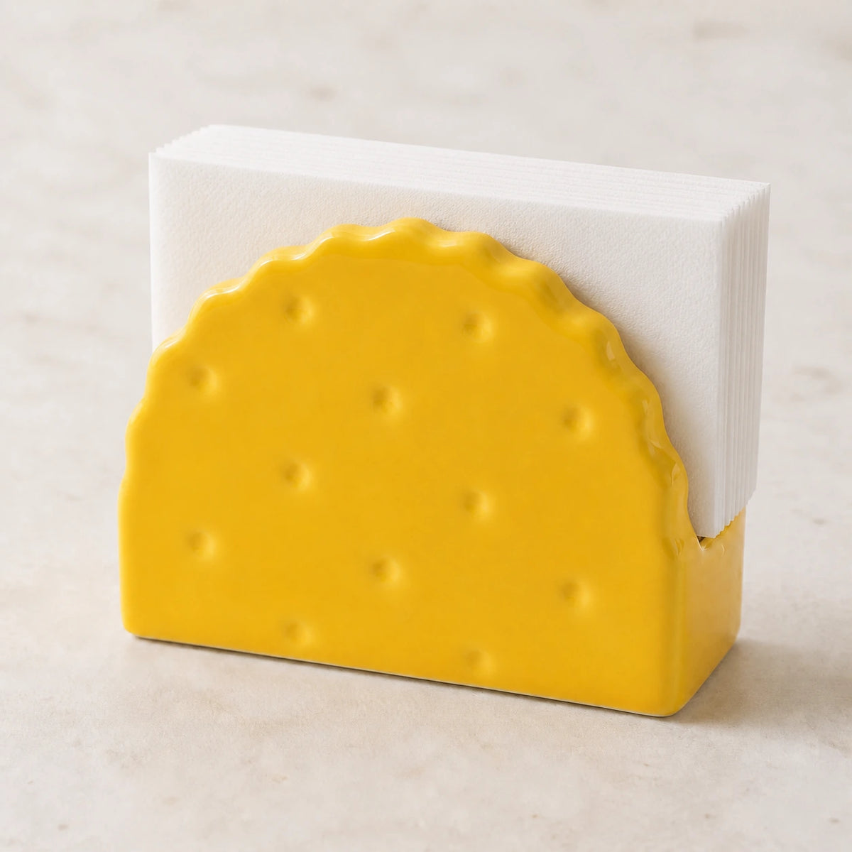 Classic Yellow Soda Cracker ceramic napkin holder with folded white napkins on pale stone
