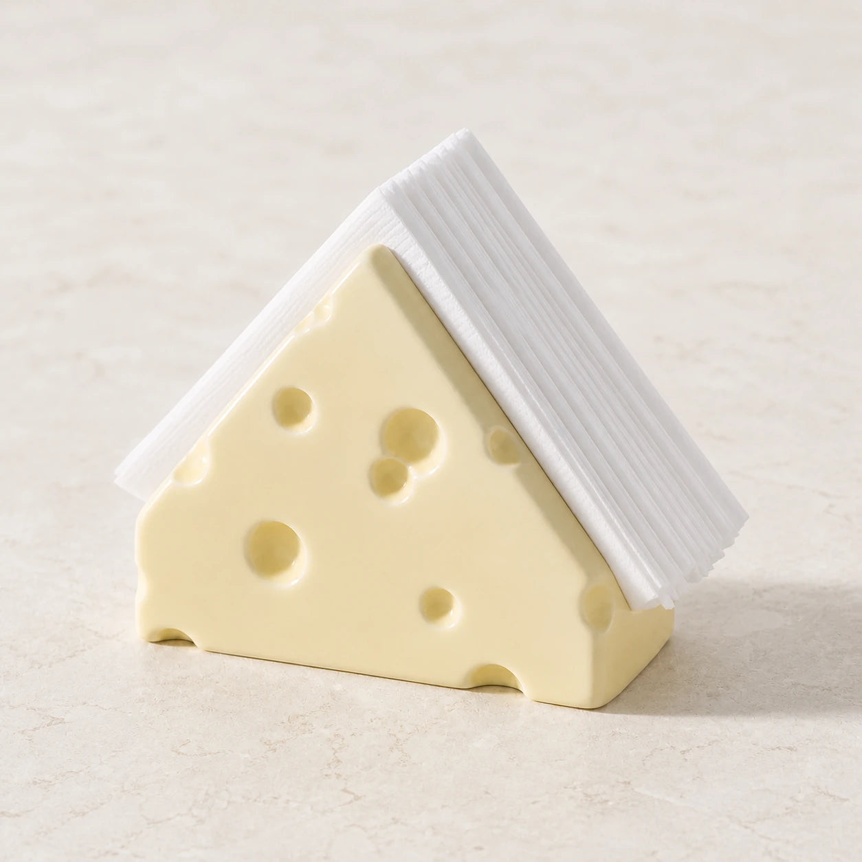 Butter Cream Swiss Cheese ceramic napkin holder with folded white napkins on pale stone
