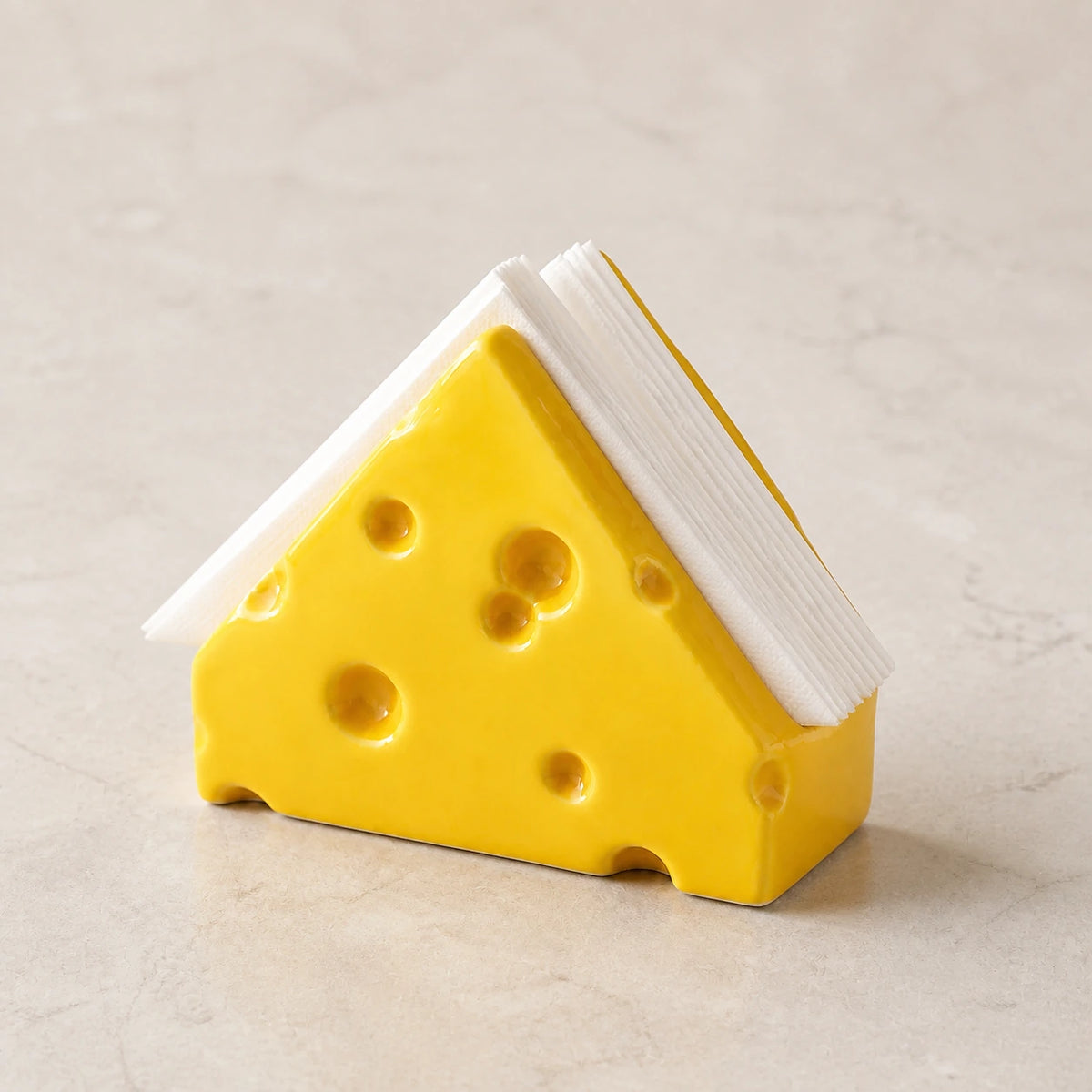 Classic Yellow Swiss Cheese ceramic napkin holder with folded white napkins on pale stone