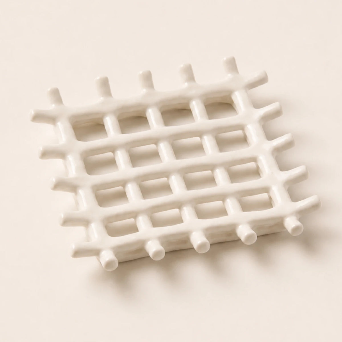 Porte-savon carré en céramique blanche mate aux tiges croisées en treillis sur fond ivoire chaleureux