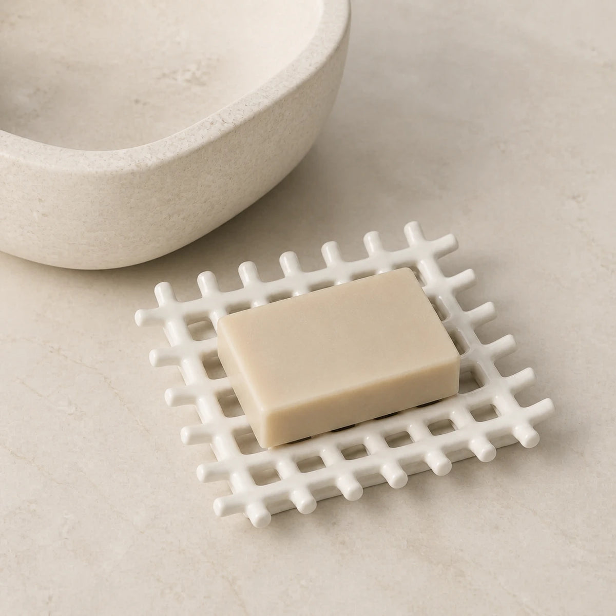 Porte-savon ajouré blanc mat avec un savon rectangulaire sur une surface en pierre près d’une vasque