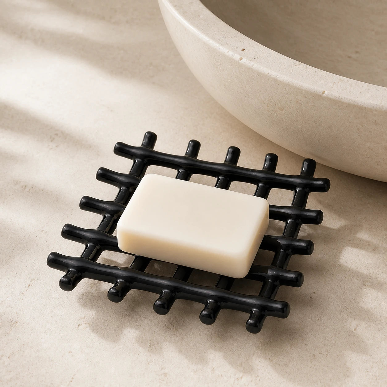 Porte-savon ajouré noir brillant avec savon rectangulaire sur un rebord en pierre près d’une vasque