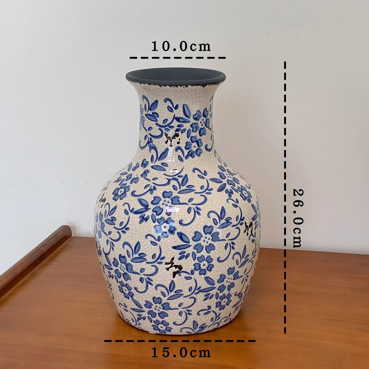 Ceramic vase with blue floral patterns on a wooden surface, with measurements indicated.